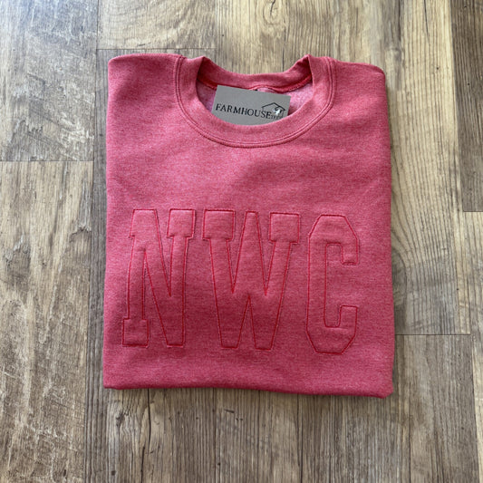 Folded pink sweatshirt with 'NWC' embroidery on a wooden surface