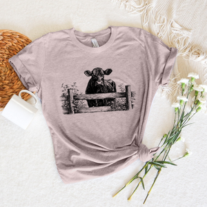 mauve t-shirt with a cow graphic at a fence with flowers 