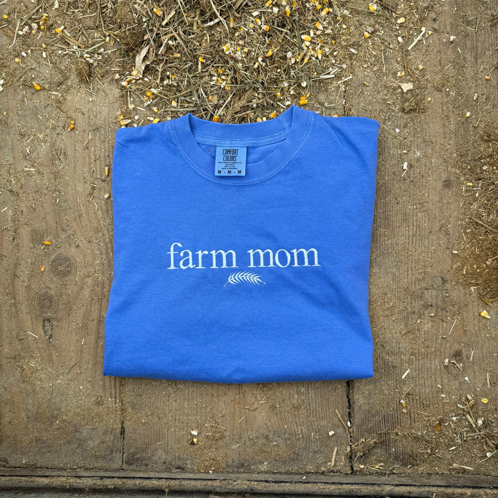 Blue t-shirt with 'farm mom' text on a wooden surface