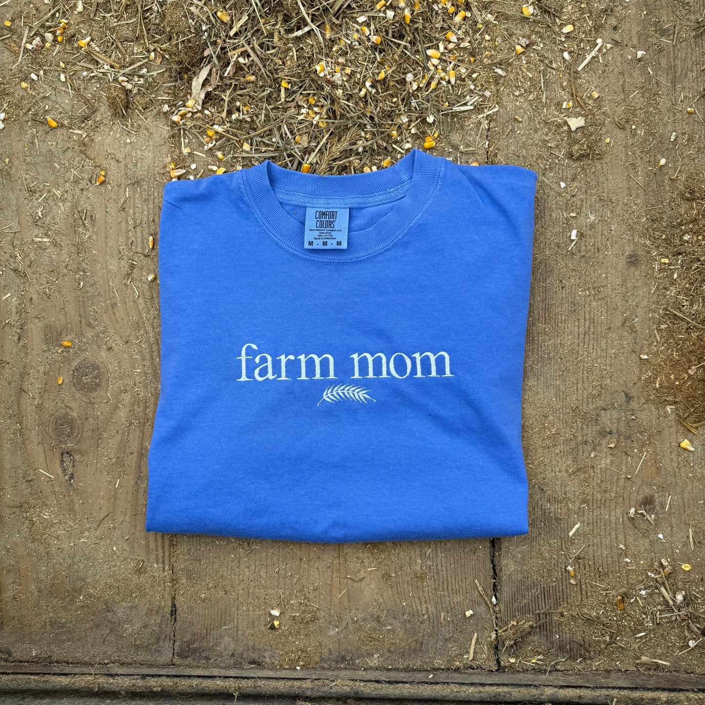 Blue t-shirt with 'farm mom' text on a wooden surface
