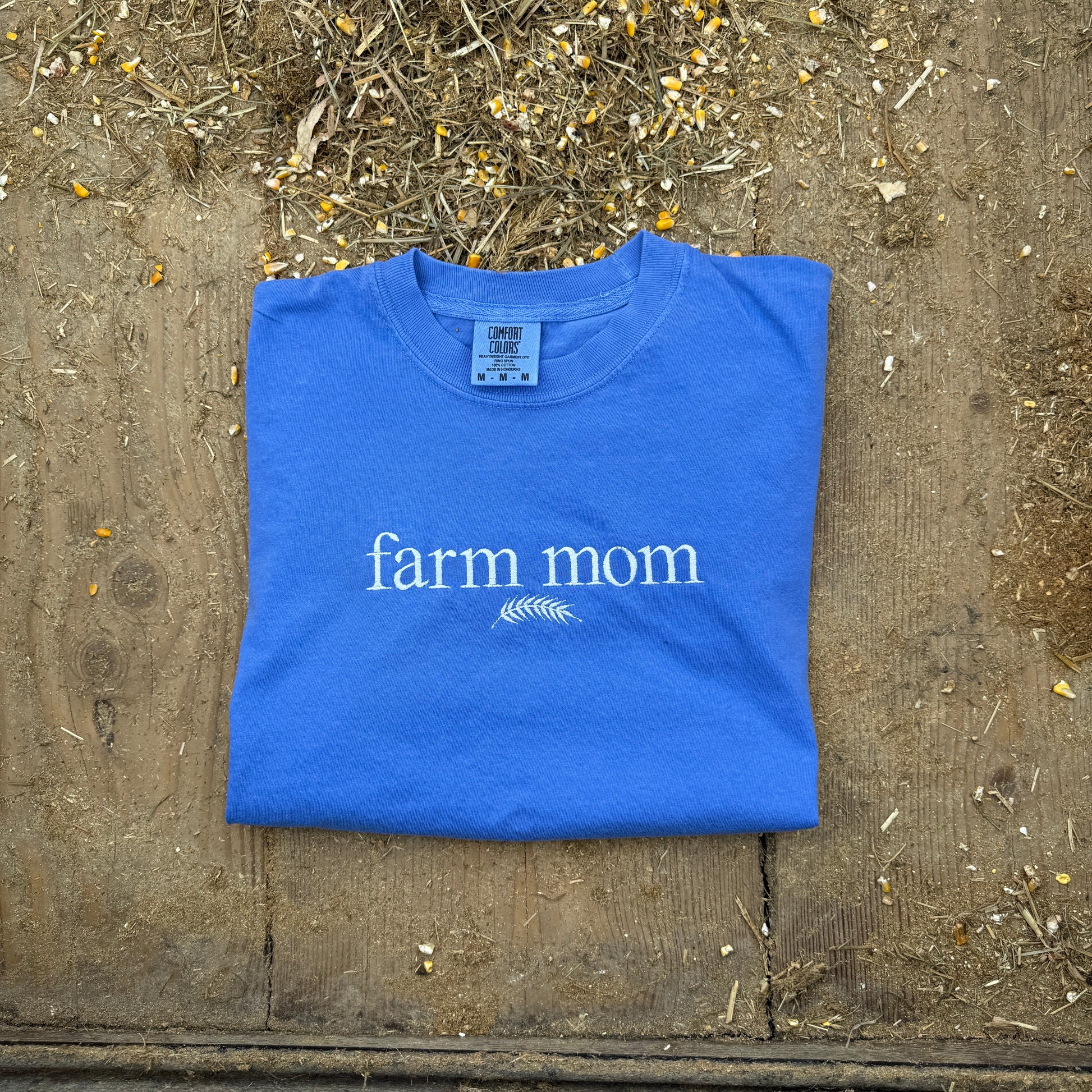 Blue t-shirt with 'farm mom' text on a wooden surface