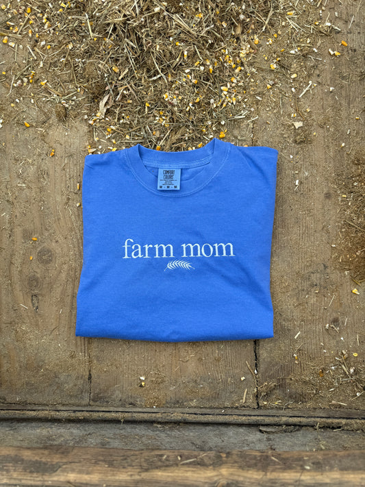 Blue t-shirt with 'farm mom' text on a wooden surface