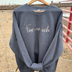 A gray crewneck sweatshirt with the text 'Farmerish' embroidered on the front, displayed on a wooden hanger against a rustic background.