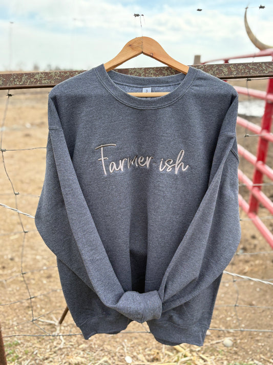 A gray crewneck sweatshirt with the text 'Farmerish' embroidered on the front, displayed on a wooden hanger against a rustic background.