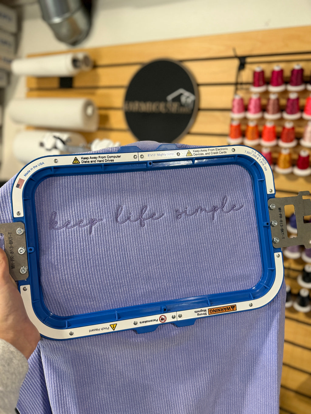 lavender sweatshirt with 'keep life simple' text held by a person in a store setting