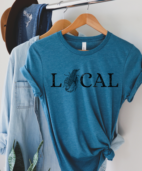 Blue t-shirt with 'LOCAL' print on a hanger against a white wall.