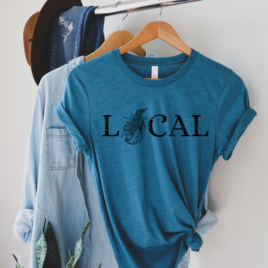 Blue t-shirt with 'LOCAL' print on a hanger against a white wall.