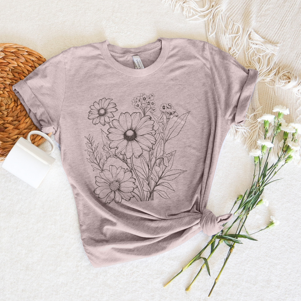 light pink t-shirt with floral design on a textured surface with flowers and a woven basket.