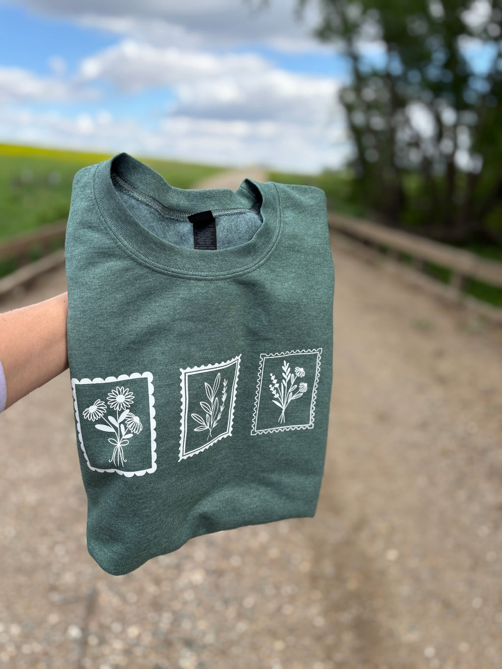 Green t-shirt with white floral designs held outdoors