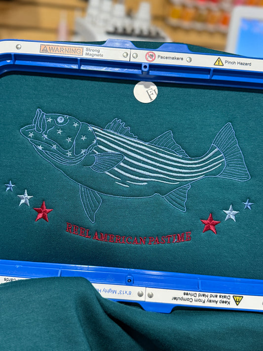 Embroidery design of a fish with stars on a green surface, featuring text ' reel American Pastime'.
