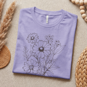 Folded purple t-shirt with floral design on a beige surface with natural elements.
