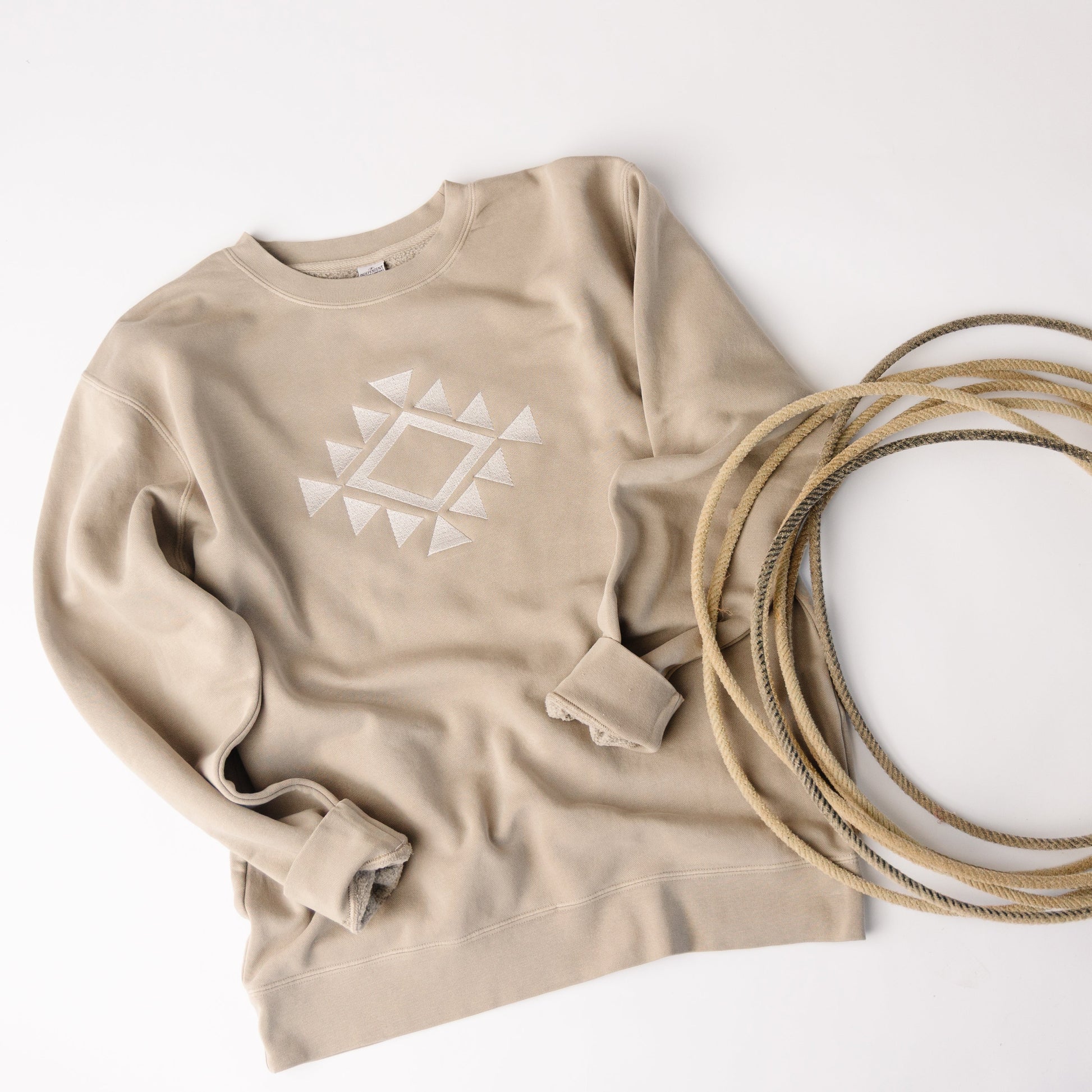 Beige sweatshirt with geometric design and coiled beige rope on a white background