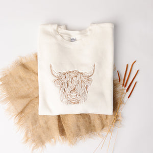 White sweatshirt with a highland cow design on a light gray background