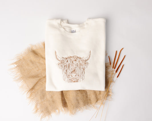 White sweatshirt with a highland cow design on a light gray background