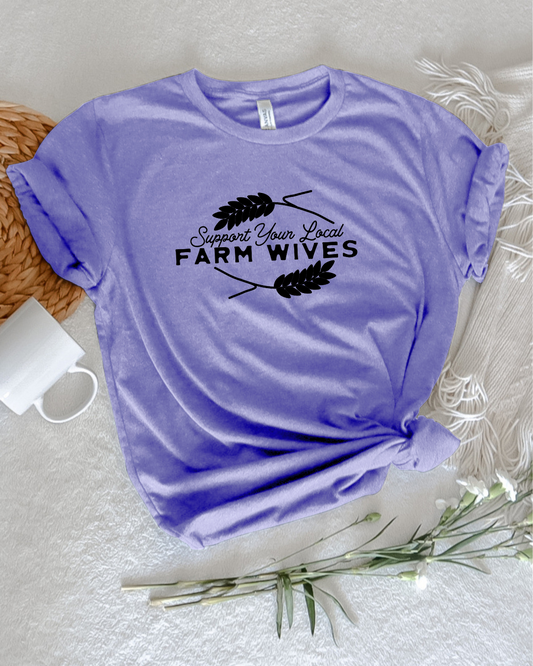 Woman in a garden holding an orange bucket, wearing a blue shirt with text 'support your local farm wives'.