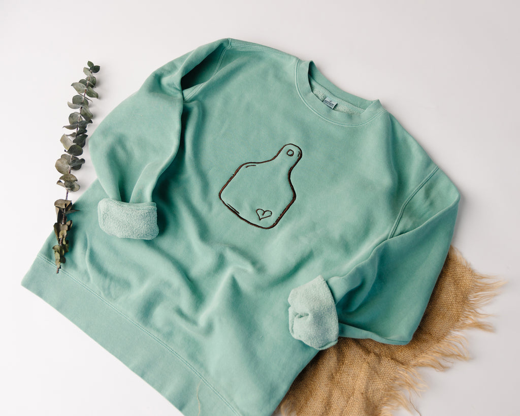 mint sweatshirt with a design on a white surface with decorative elements.