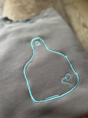 brown  fabric with teal embroidered design of a heart on a cattle tag