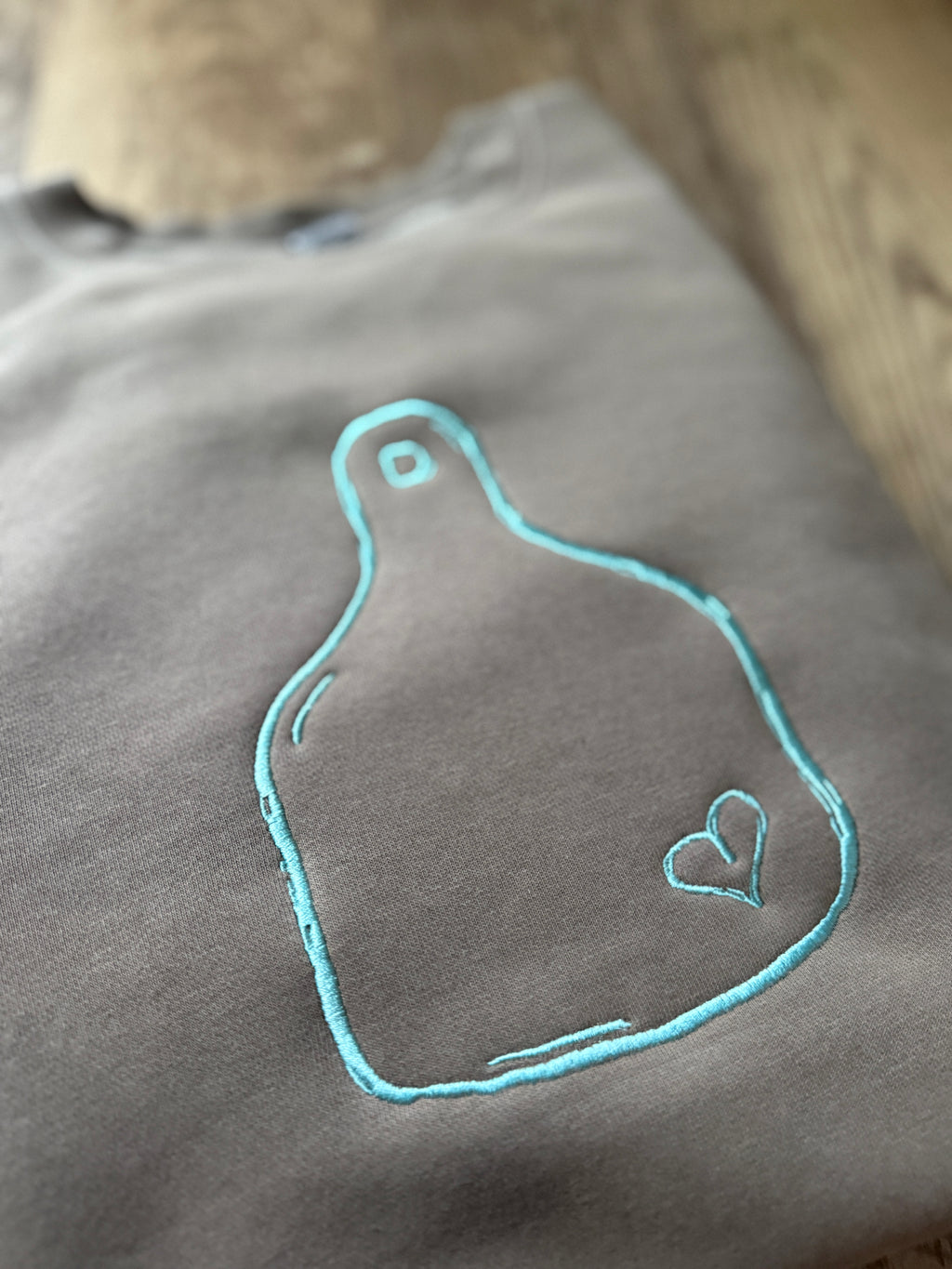 brown  fabric with teal embroidered design of a heart on a cattle tag