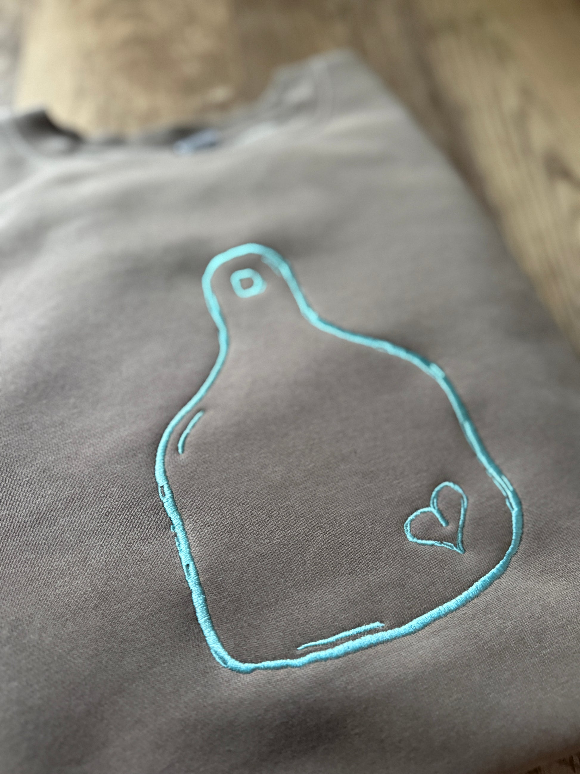 brown  fabric with teal embroidered design of a heart on a cattle tag