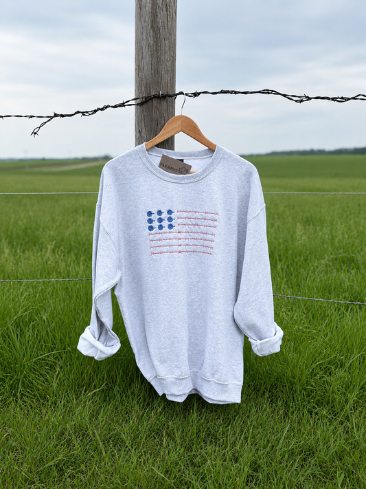 White sweatshirt with a patriotic graphic design on a hanger against a green field background