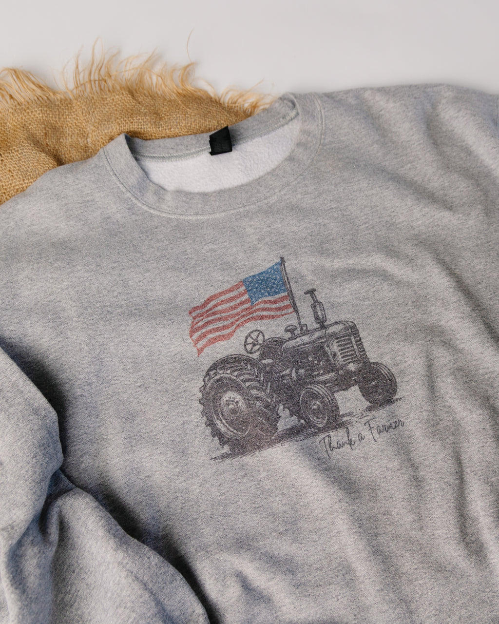 Gray sweatshirt with a tractor and American flag design on a textured surface.