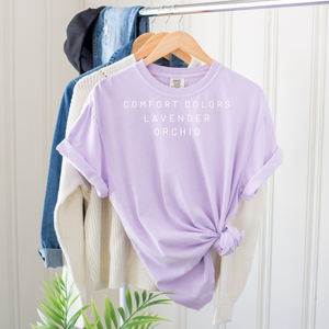 Lavender t-shirt on a hanger with 'Comfort Colors' text against a white wall.