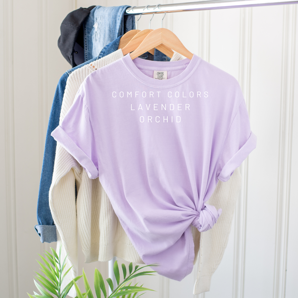 Lavender t-shirt on a hanger with 'Comfort Colors' text against a white wall.