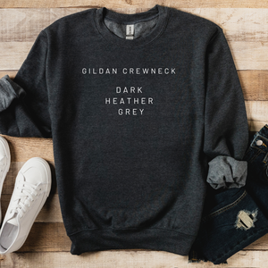 Dark heather gray sweatshirt with 'Gildan Crewneck Dark Heather Grey' text on a wooden surface with white sneakers and jeans.