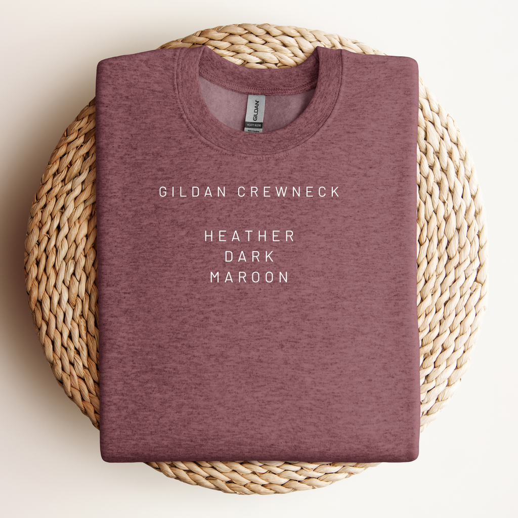 Folded maroon sweatshirt with 'Gildan Crewneck Heather Dark Maroon' text on a woven mat.