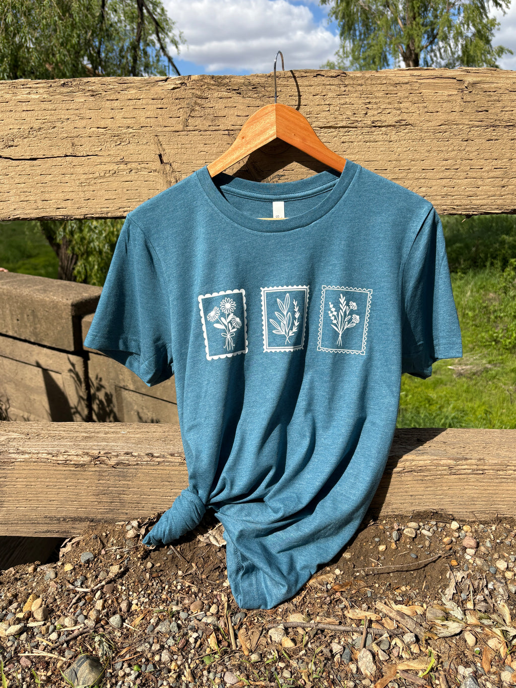 Blue t-shirt with white floral graphics on a wooden post outdoors