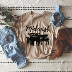 A beige Bella Canvas T-shirt with 'Midwest' text and a cattle design, accompanied by a pair of blue jeans, a blue scarf, and brown boots, all laid out on a white surface with a patterned background.
