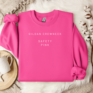 Pink Gildan crewneck sweatshirt on a textured surface with a cup and decorative elements.