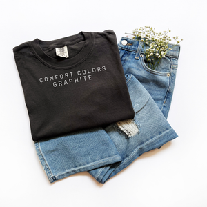 Folded black t-shirt with 'Comfort Colors Graphite' text on a white background
