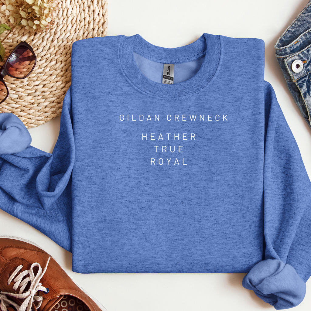 Folded blue sweatshirt with 'Gildan Crewneck Heather True Royal' text on a white surface with accessories.
