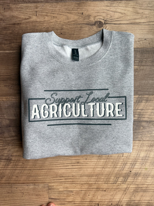 Woman holding a red bowl in a garden with a building in the background support your local ag shirt