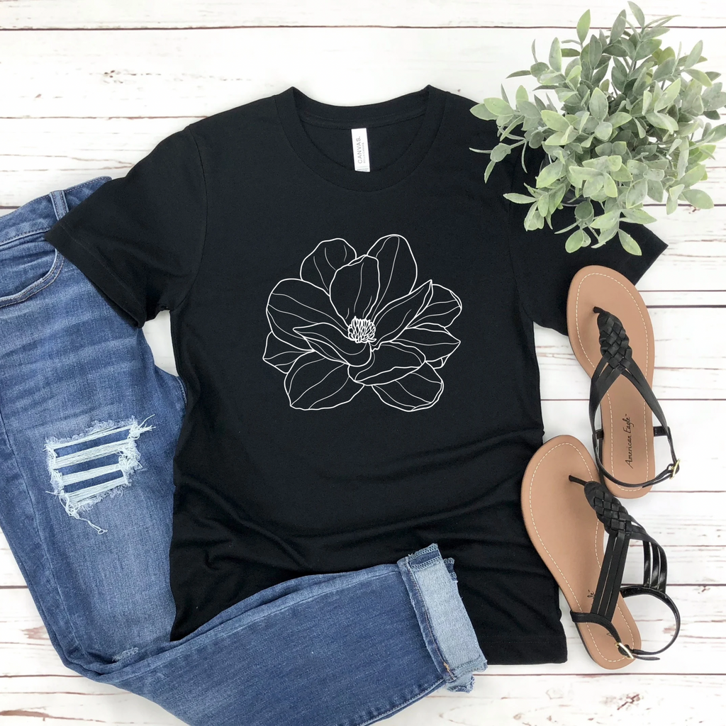 Black t-shirt with floral design, paired with denim jeans and sandals on a wooden surface.