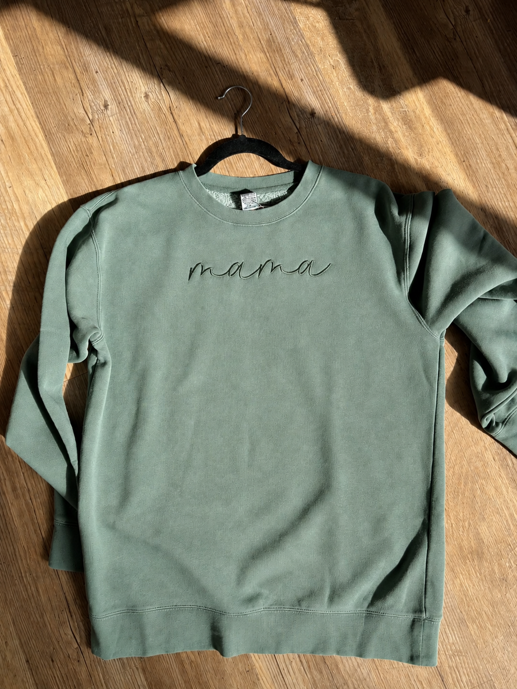 Green sweatshirt with 'mama' text on a wooden surface