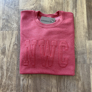 Folded pink sweatshirt with 'NWC' embroidery on a wooden surface